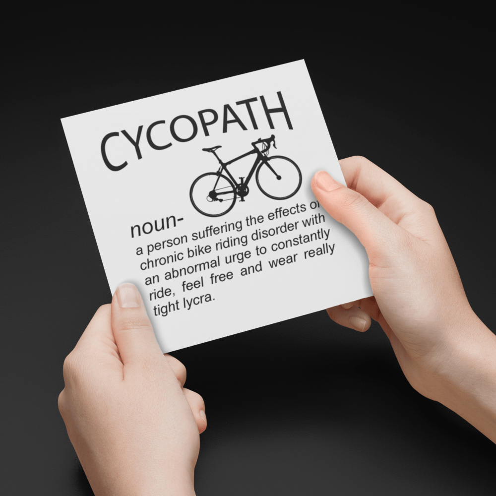 Hands holding a greeting card with the word 'Cycopath' and a bicycle illustration on a black background