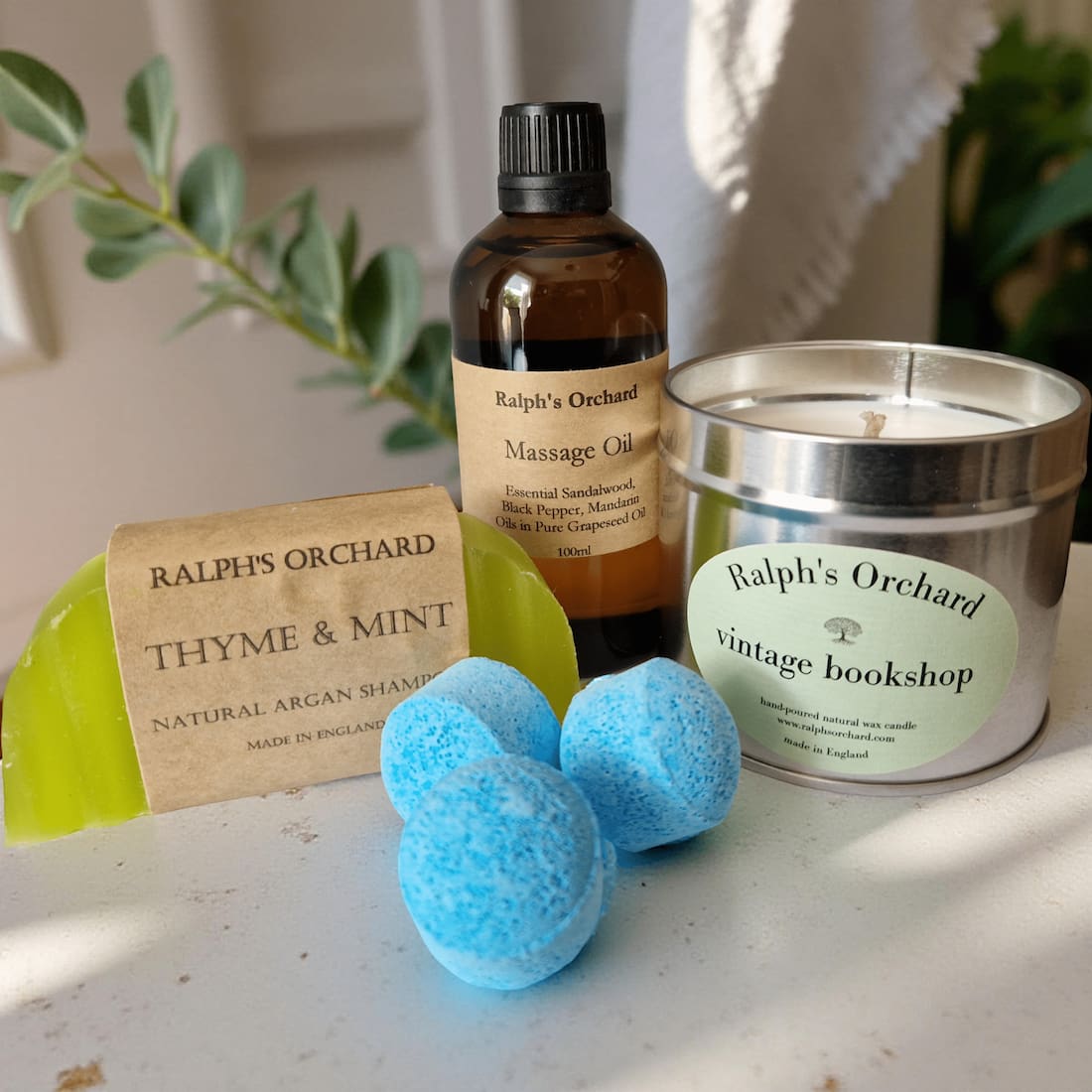 Collection of Ralph's Orchard products, including a candle, oil, shampoo bar, and bath bombs on a surface.