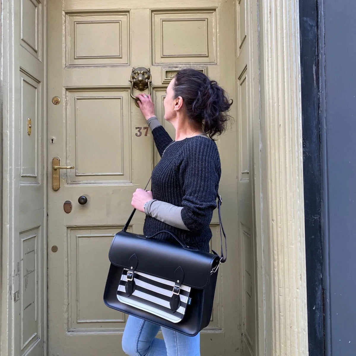Model wearing the Zatchels Gothic striped leather satchel over one shoulder outside a doorway