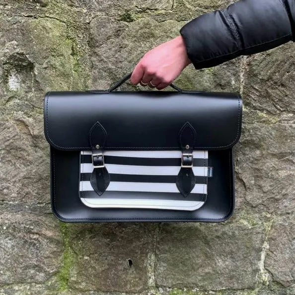 Zatchels Gothic black-and-white striped leather satchel held by its top handle against a stone wall.