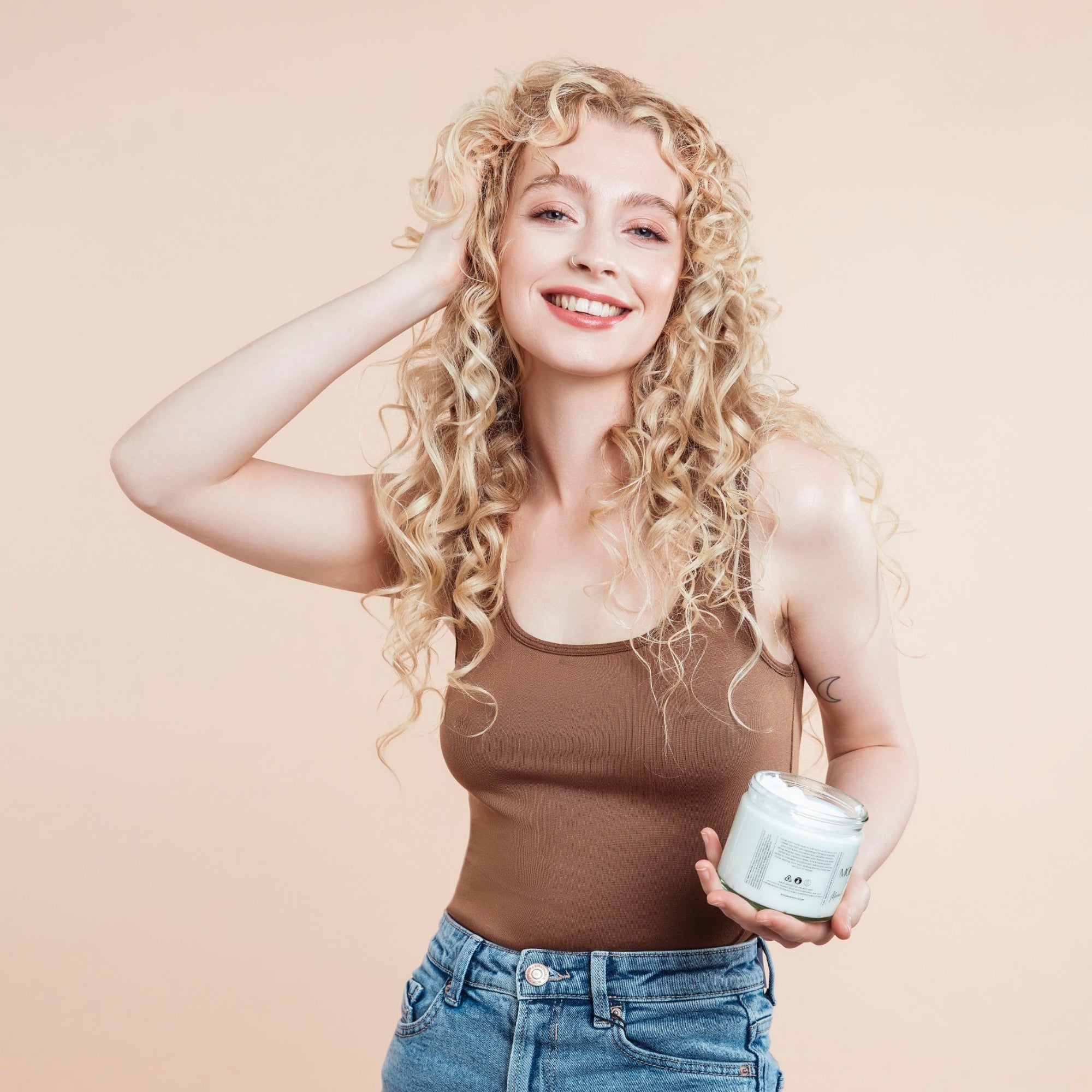 Woman with curly hair holding a jar against a beige background