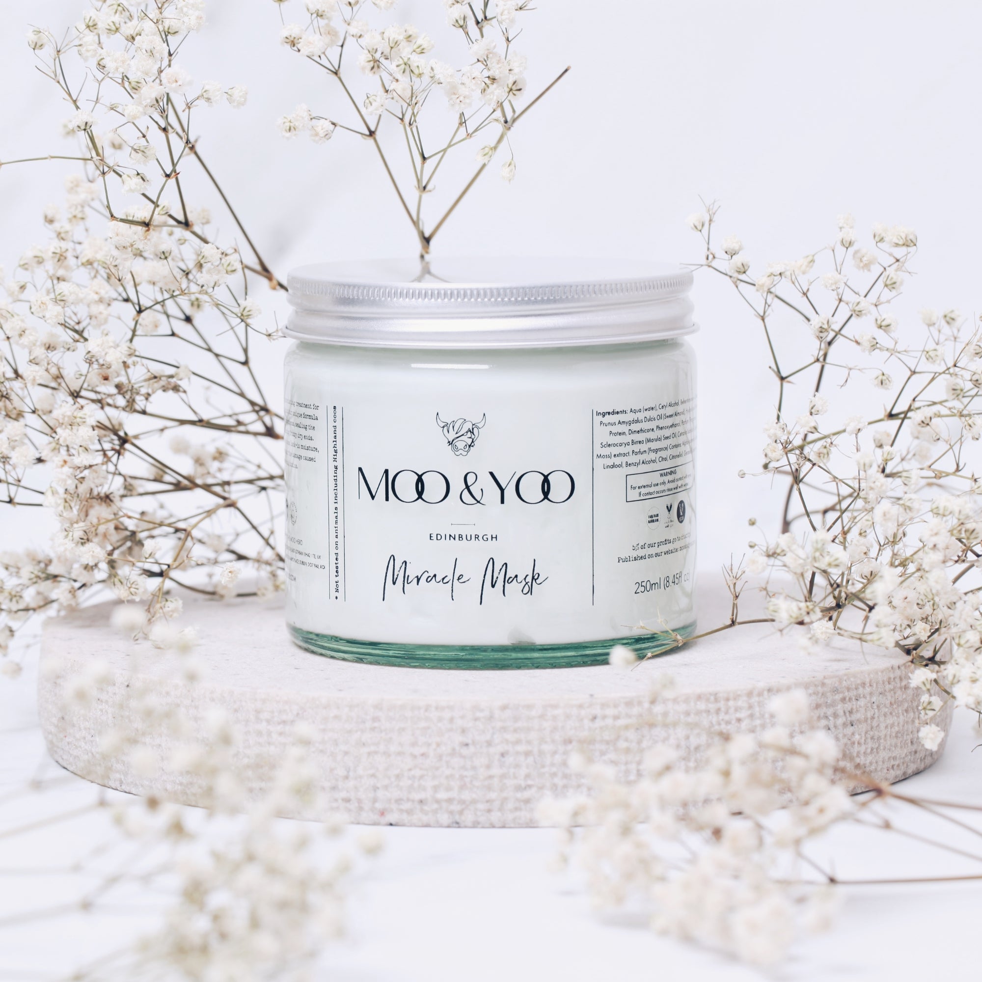 Jar of 'Moo & Yoo' Miracle Mask with white flowers on a light background
