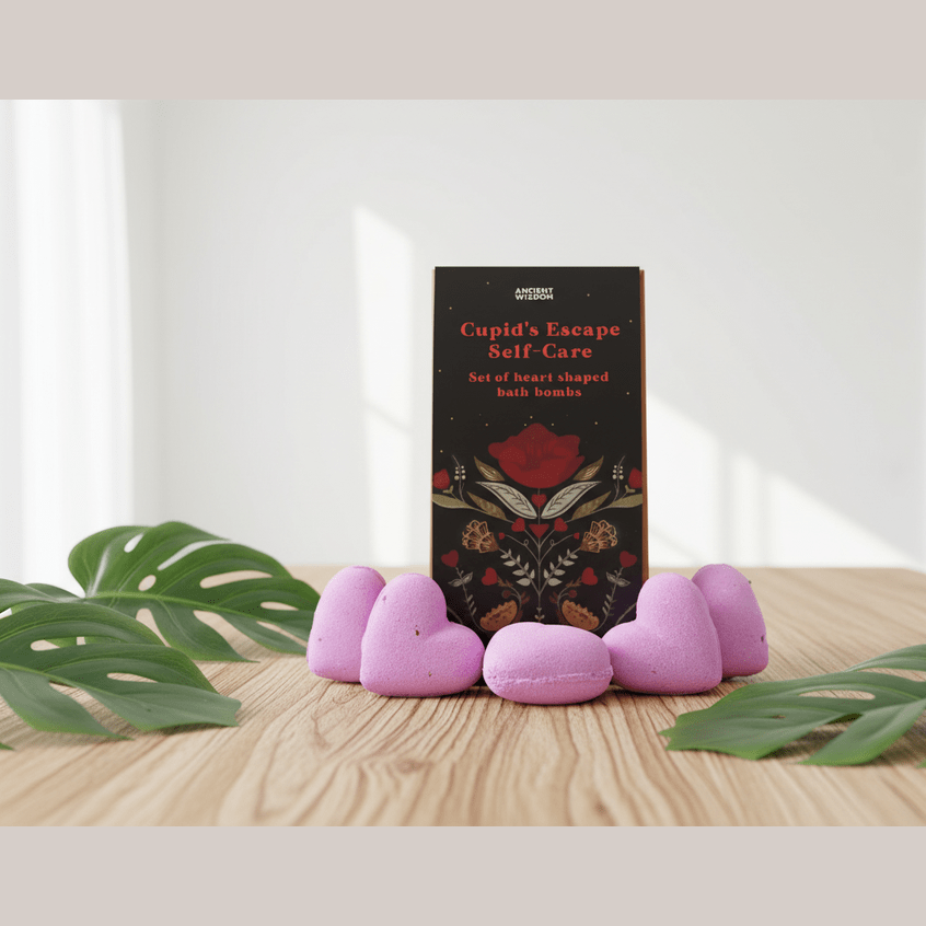 A gift set titled 'Cupid's Escape Self-Care' with pink heart-shaped bath bombs on a wooden surface with green leaves.