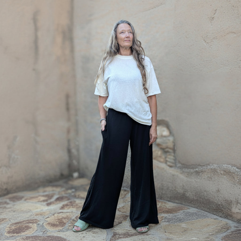 Person wearing a white t-shirt and black pants standing against a textured wall.