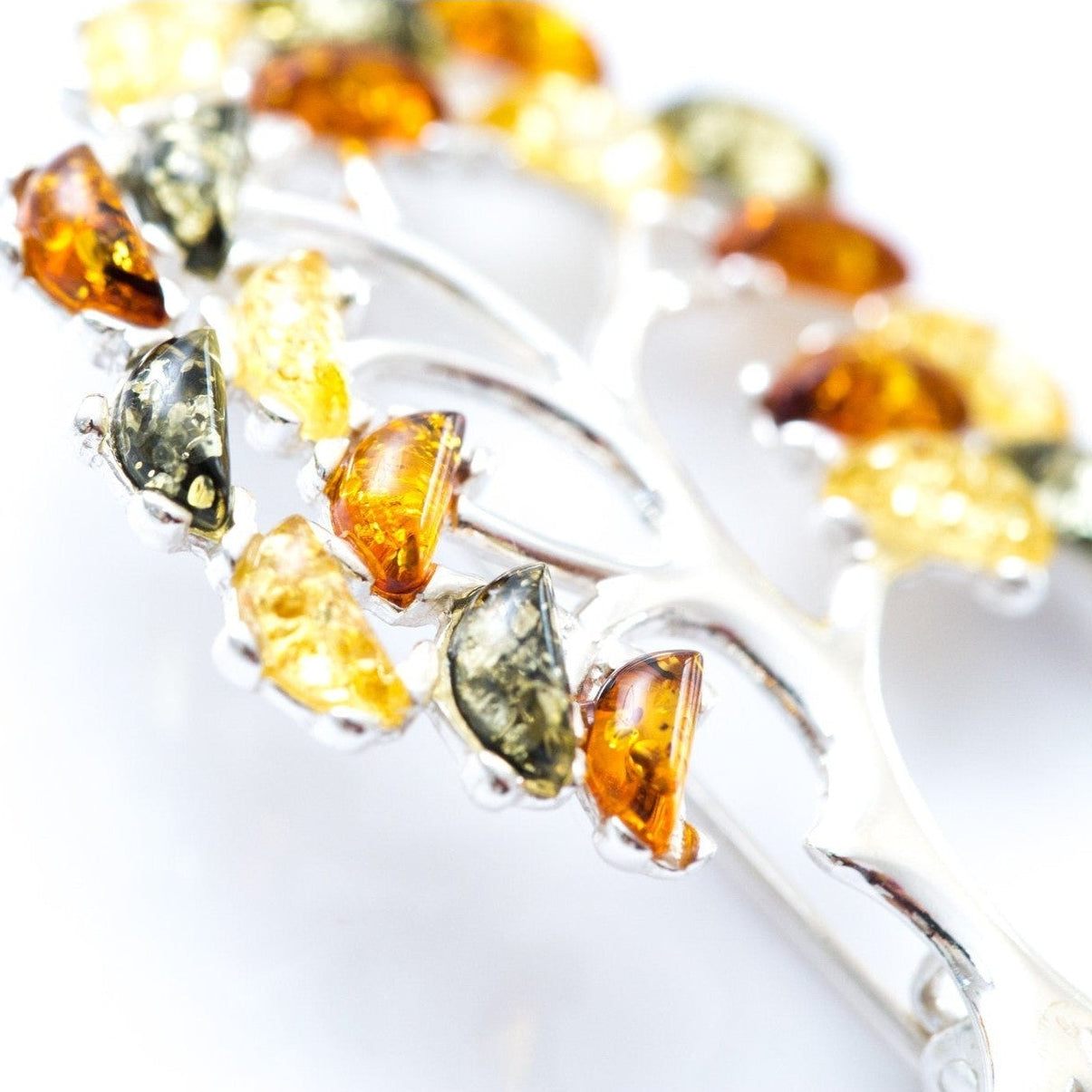 Silver brooch with amber-colored stones on a white background
