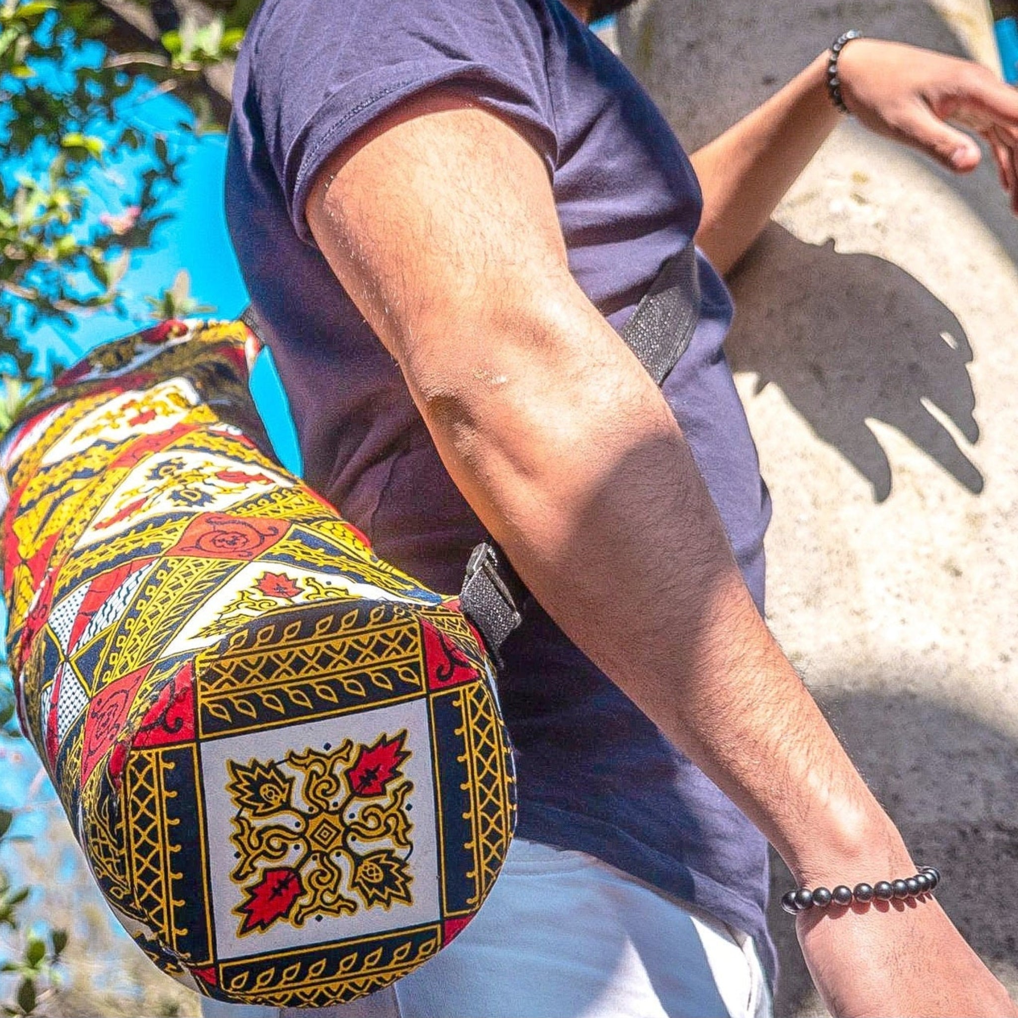 Person holding a colourful yoga mat bag with intricate patterns outdoors.