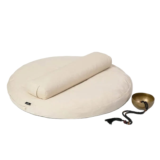 Beige meditation cushion with a small bowl and prayer wheel on a white background