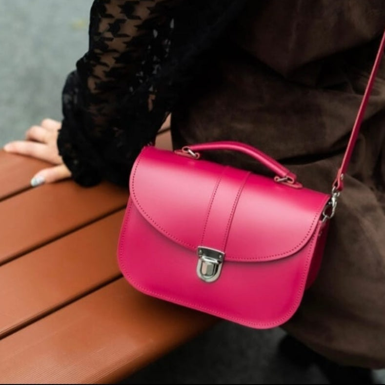 Magenta Zatchels Olympia leather handbag worn crossbody by a person seated on a wooden bench