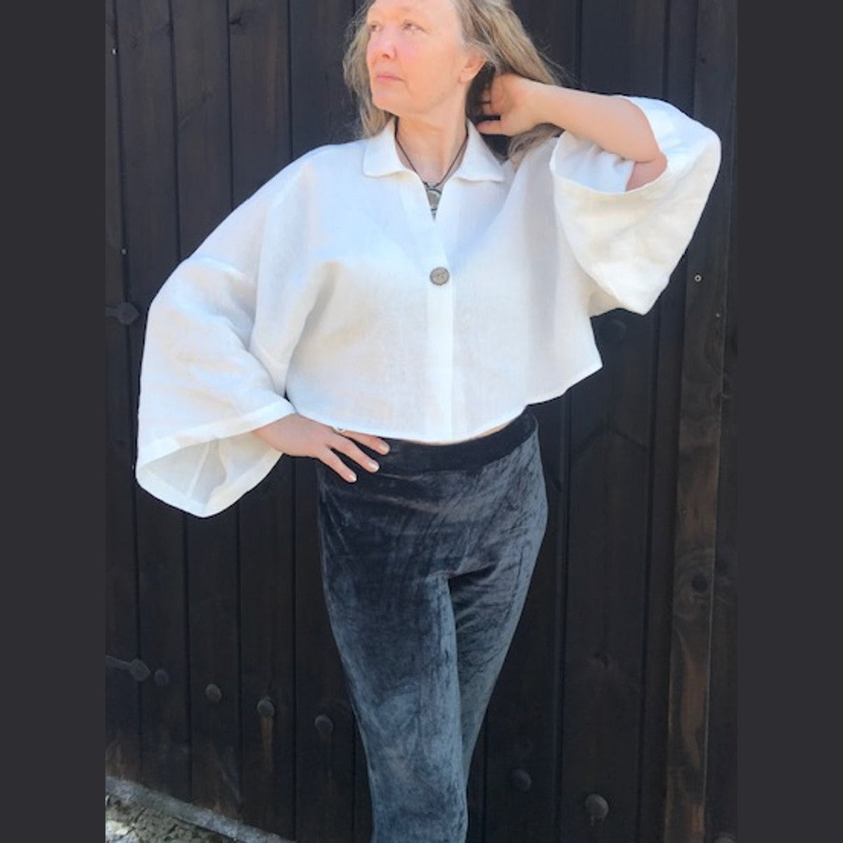 Person wearing a white blouse with wide sleeves and gray pants against a dark wooden background