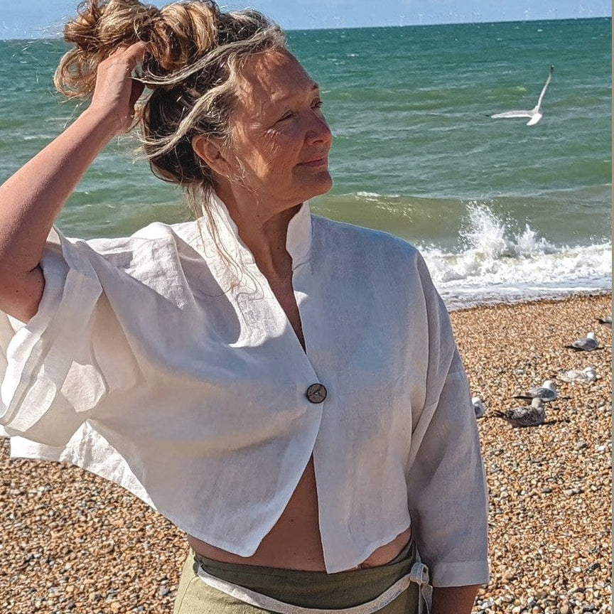 Person on a beach wearing a white shirt and green pants with ocean and sky in the background