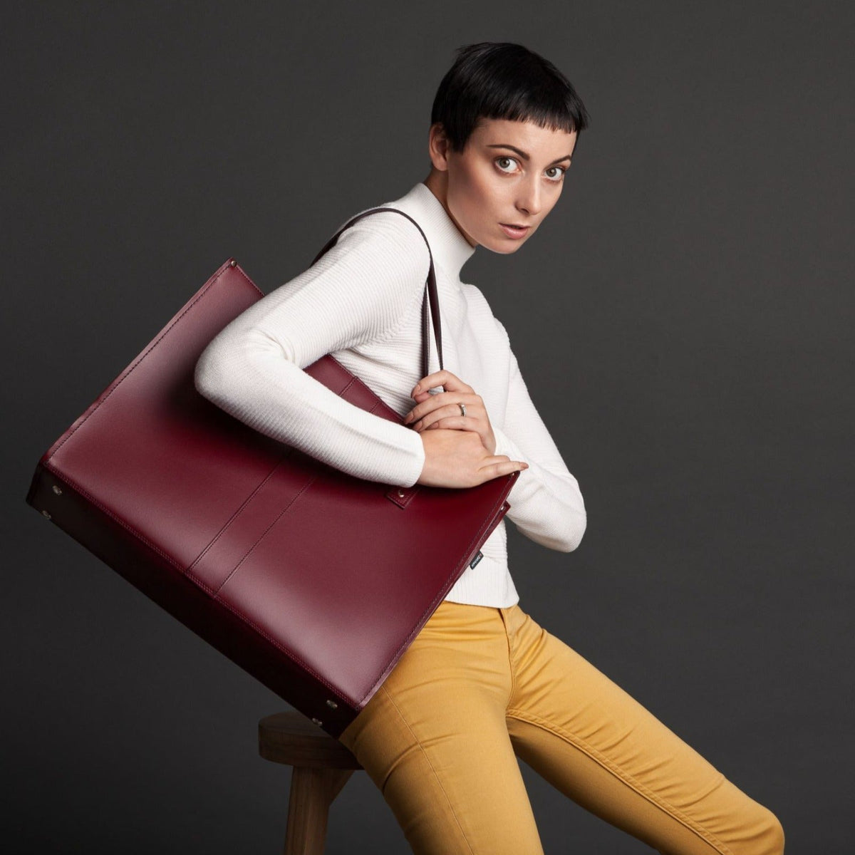 Woman holding a large red-brown leather bag against a dark background