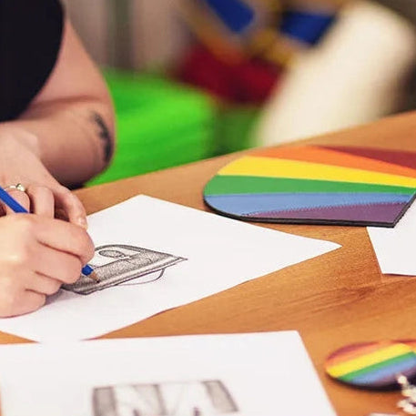 Pride collection design sketches and rainbow leather pieces on a workshop table
