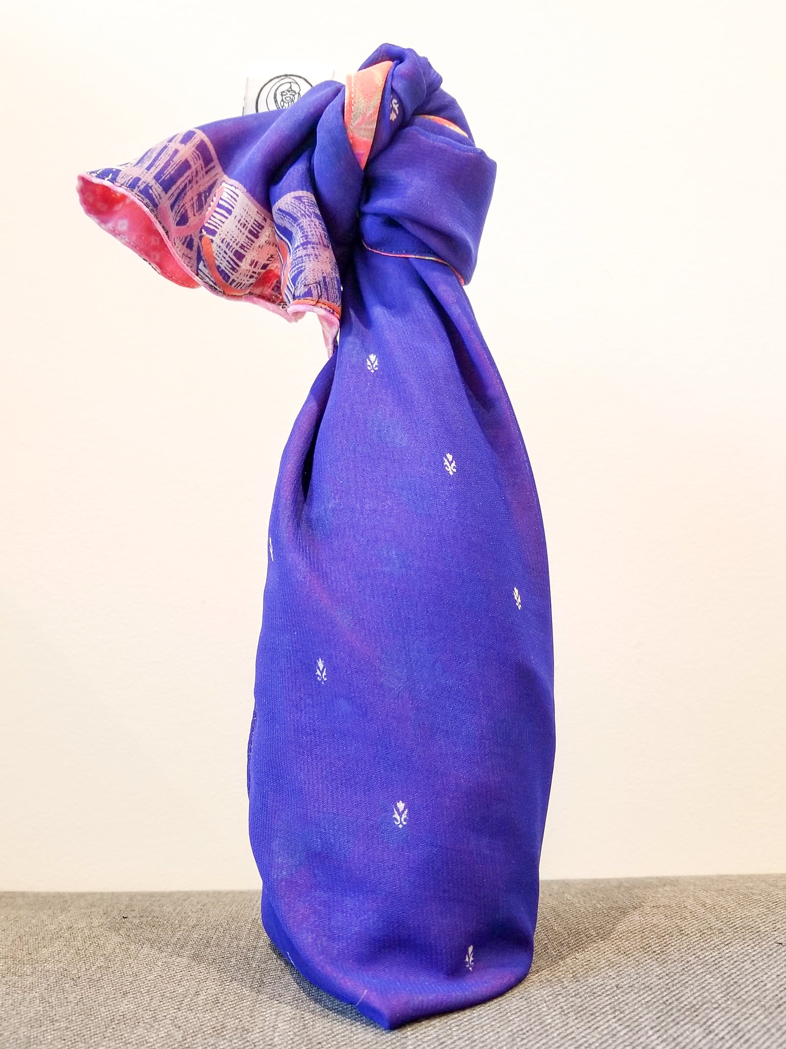 Purple fabric wrapped around a bottle with a decorative pattern on a beige background