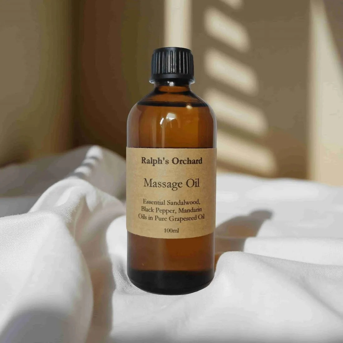 Bottle of Ralph's Orchard Massage Oil on a white surface with a blurred background