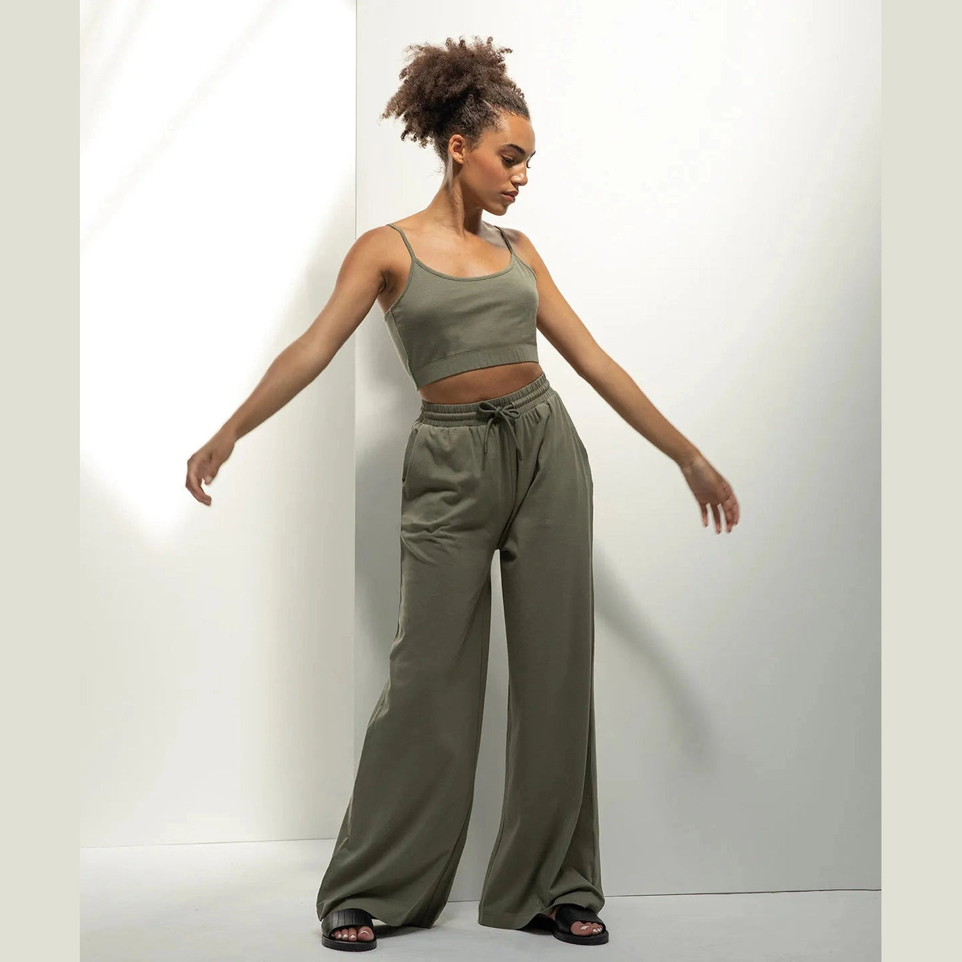 Woman wearing a green tank top and wide-leg pants against a white background