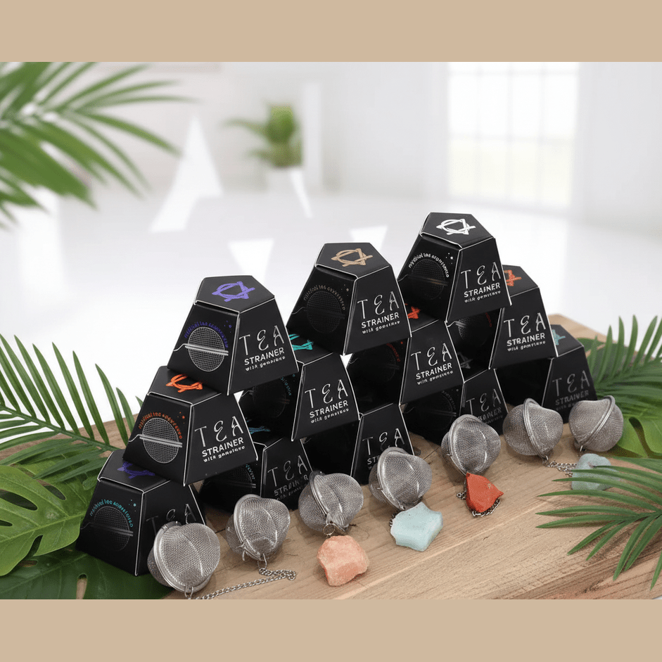 Tea infusers in pyramid shapes with various colors on a wooden board surrounded by green leaves.