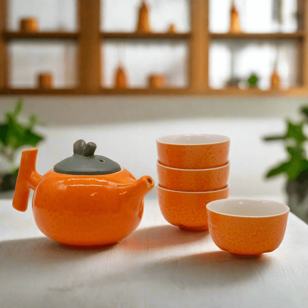 Emmy Jane - Herbal Teapot Set - Orange Teapot & Four Cups. This charming set features a teapot shaped like a plump orange and four matching cups with a textured orange peel design. The vibrant design and compact size make it the perfect gift.